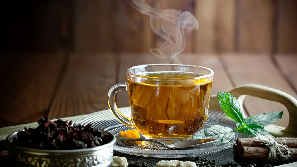 Hot herbal tea in a glass cup on a platter garnished with tea leaves and cinnamon sticks
